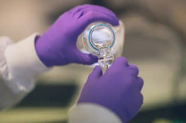 Lab technician wearing purple gloves pouring liquid into a container